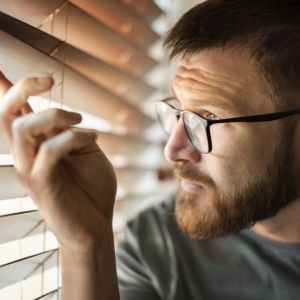 mężczyzna patrzy przez żaluzje